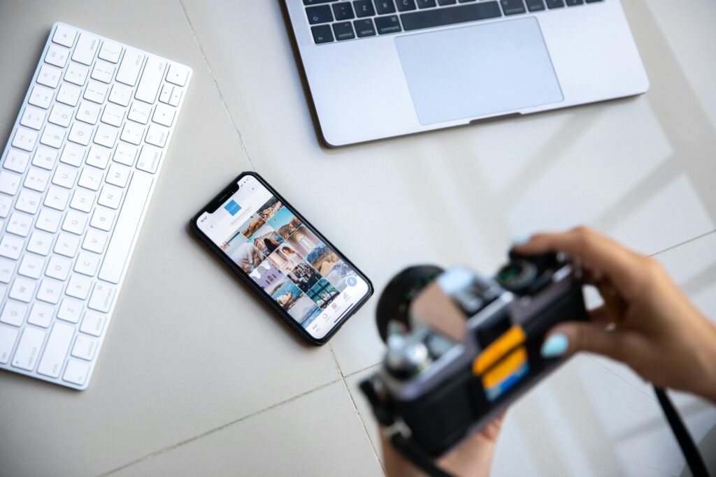 pexels-photo-4549411-4549411 Person using vintage camera with smartphone and laptop in creative setup.