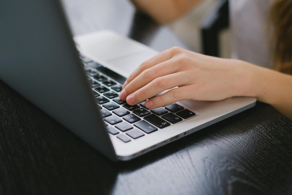 pexels-photo-7561704-7561704 Close-up of a hand typing on a laptop keyboard placed on a wooden desk.