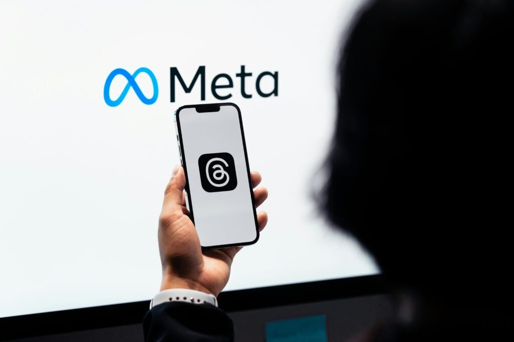 pexels-photo-17614479-17614479 Hands holding smartphone with Meta Threads logo on screen, Meta branding in background.
